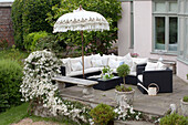 Outdoor seating with white parasol and watering can on terrace of Sussex country house, England, UK