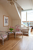 Ein Paar gepolsterte Stühle mit Beistelltisch unter der Treppe eines Landhauses in Sussex, England, UK