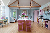 Pastel pink and blue open plan kitchen with beamed ceiling in Sussex country house, England, UK