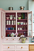 Tableware in pastel pink storage dresser in Sussex country house, England, UK