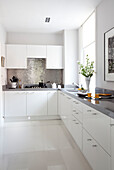 White fitted kitchen with metallic splashback in London apartment, UK