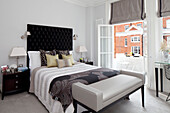 Bett mit schwarzem Kopfteil mit Knöpfen in einem Zimmer mit offenen Türen zum Balkon, Londoner Wohnung, UK