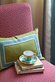 Teacup and books with applique cushion on upholstered chair in London bedroom, England, UK
