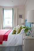 Red blankets in bedroom with sash window in London townhouse, England, UK