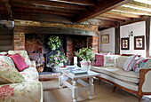 Sofas in front of exposed brick fireplace in beamed living room in Maidstone farmhouse, Kent, England, UK