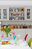 Cut tulips and place settings on table with kitchen storage in Surrey country home England UK