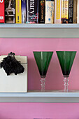 Green goblets and books on shelves set against pink wall in Sussex home, England, UK