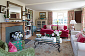 Rosa und weiße Sofas mit grünem Sessel und Couchtisch mit Glasplatte im Wohnzimmer eines Hauses in Sussex, England, UK