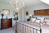 White chandelier above brass bed with tapestry in Sussex home, England, UK