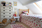 Rose patterned bedspread below dormer window in attic bedroom in Dorset cottage, England, UK