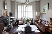 Brown leather sofa with a pair of vintage armchairs in living room of London townhouse, England, UK