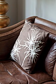 Floral patterned cushion on brown leather sofa in London townhouse, England, UK