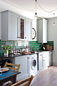 Washing machine in fitted kitchen with green tiled splashback, London home, England, UK
