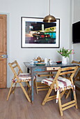 Artwork with brass pendant light above table with wooden folding chairs in London home, England, UK