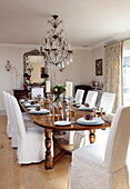 Slip cover dining chairs at table with cut glass chandelier in Kent home, England, UK