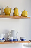 Teapots and sugar bowls on open wooden shelves in kitchen of Kent family home England UK