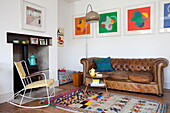 Schaukelstuhl und Holzofen mit braunem Chesterfield und moderner Kunst im Wohnzimmer eines Familienhauses in Kent, England UK