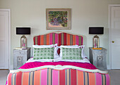 Pink and orange upholstered bed with lamps on silver bedside cabinets in Herefordshire home, England, UK