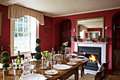 Lit fire in red dining room of Burwash home, East Sussex, England, UK