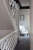 White armchair in hallway landing with trellis banister, West Sussex home, England, UK