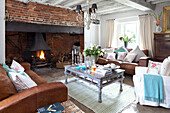 Brown leather sofas and coffee table in living room with exposed brick fireplace in West Sussex home England UK