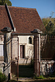 Blick durch das schmiedeeiserne Tor auf den sonnenbeschienenen Außenbereich eines französischen Ferienhauses an der Loire, Frankreich