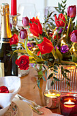 Red Christmas tulips and lit tealights on dining table in West Sussex home, England, UK