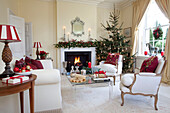 Pair of matching armchairs and lit fire with Christmas tree in West Sussex living room, England, UK