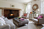 Pair of matching armchairs with velvet ottoman in front of lit woodburning stove in London home England UK