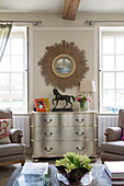 Sunburst mirror above silver chest of drawers in living room of London home England UK