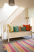 Patterned cushions on painted bench seat with striped rug in flagstone hallway in London home England UK