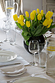 Yellow tulips with glassware on dining table in UK farmhouse