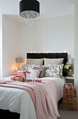 Black headboard and lampshade with pink blankets and gift wrapped presents on double bed in London home, England, UK