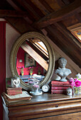 Oval shaped mirror with bust and hardbacked books on bedroom chest in French farmhouse bedroom