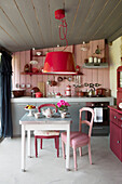 Roter Hängelampenschirm über einem Küchentisch mit Teekanne und Tassen in einem bretonischen Landhaus, Frankreich