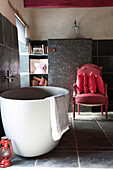Freestanding bath and red armchair in bathroom tiled with slate, Brittany cottage, France