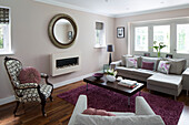 Pastel pink living room with circular mirror and corner sofa in London family home, England, UK