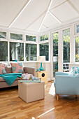 Light blue armchair with sofa in conservatory extension of London family home, England, UK