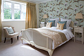 painted wicker footboard in bedroom with iris patterned wallpaper, London family home, England, UK