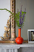 Cut flowers in orange vase on marble mantlepiece in Oxfordshire home England UK