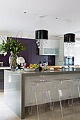 Transparente Barhocker an der Frühstücksbar mit lila Spritzschutz in einer Küche in Berkshire, England, UK