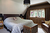 Quilted double bed with travelling chest at leaded window in London bedroom, UK