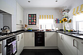 Modernes Kunstwerk in schwarz-weißer Einbauküche mit gelb gestreiften Jalousien in einem Londoner Stadthaus England UK