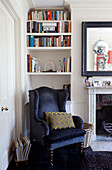 Black velvet armchair with recessed bookshelves in living room of London townhouse, England, UK