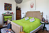 Lime green bed cover with wooden chest and colourful artwork in bedroom of London townhouse, England, UK