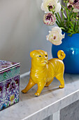 Yellow dog statue with blue vase and cut flowers on shelf in London home, England, UK