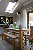 Wooden dining table with bench seats below skylight with black and gold sign in attic room of London home, England, UK
