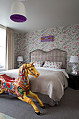 Colourful yellow rocking horse at foot of bed in room with patterned wallpaper, London home, England, UK