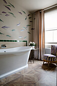 Fish swim on wall above white freestanding bath in London home, England, UK