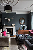 Buttoned ottoman and sofa with vintage mirror and antlers in Sussex living room, England, UK